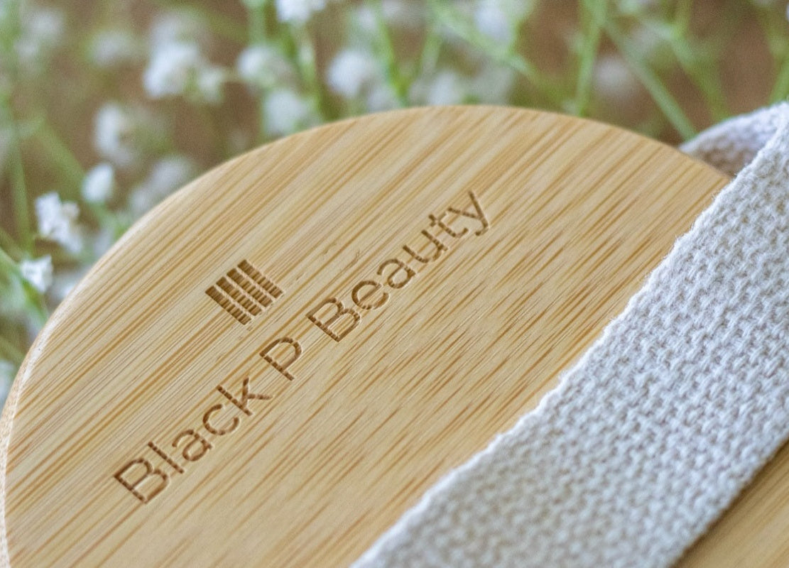 Wooden face brush with 'Black P Beauty' branding against a blurred floral background