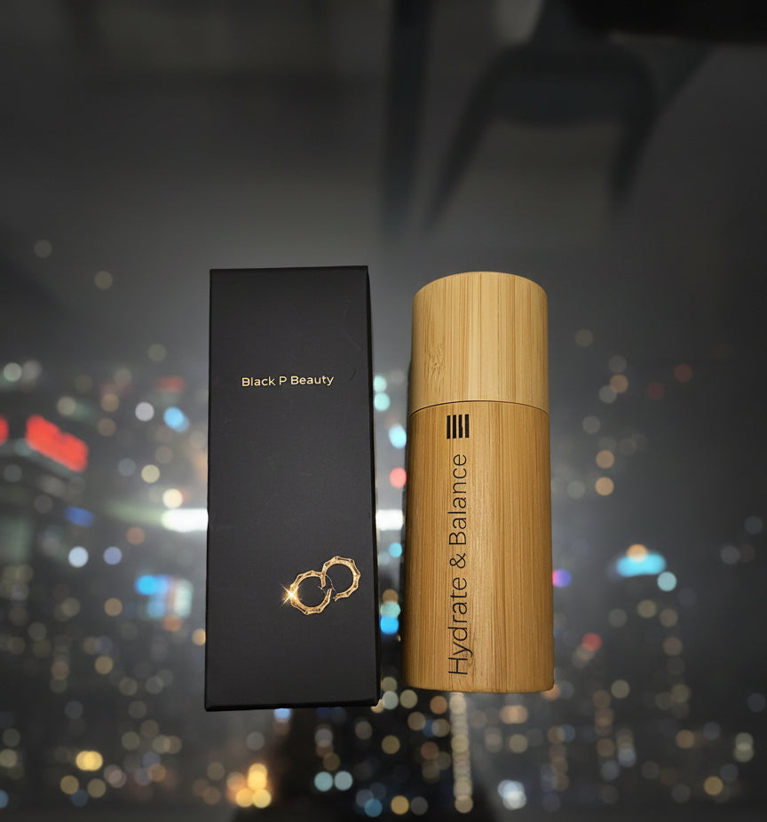 Bamboo bottle labeled 'Hydrate & Balance' next to a black box labeled 'Black P Beauty' on a glass table