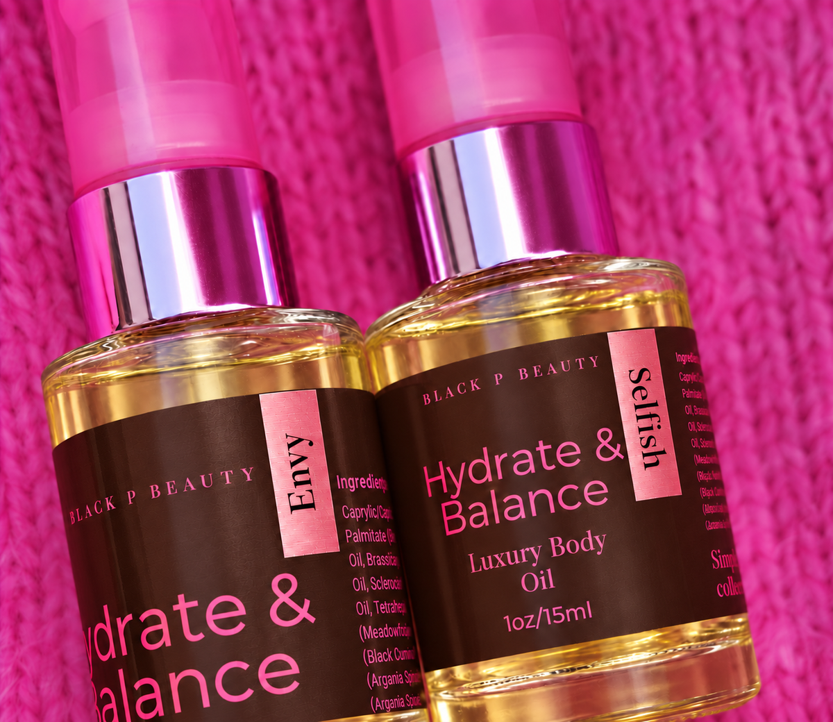 Two bottles of Black P Beauty body oil, including Envy and Hydrate & Balance Luxury Body Oil, with pink caps and dark brown labels, set against a textured hot pink background.
