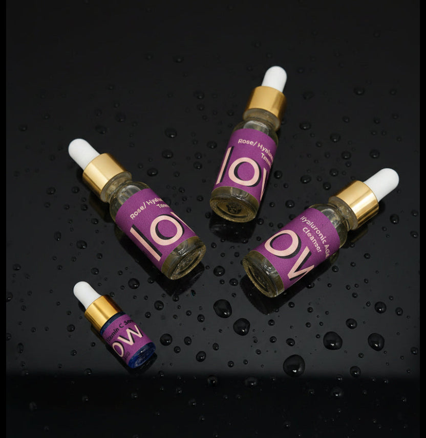 Four skincare serum bottles with purple labels and gold caps on a white background